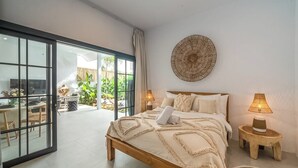 Une chambre dotée d’un grand lit, de deux lampes de chevet, d’une décoration murale et d’une porte-fenêtre coulissante donnant sur un balcon aménagé avec du mobilier d’extérieur.