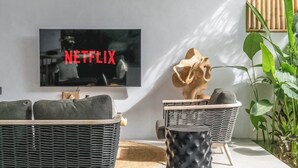 Un salon moderne doté d’un téléviseur à écran plat affichant le logo « NETFLIX », d’un canapé en osier, d’une table basse ronde et d’un paravent en bambou.