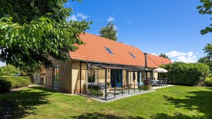 A house with a red-tiled roof, a glass-enclosed patio, and a well-maintained lawn. - Group home in Andijk with garden room (Andijk)