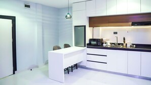Una cocina moderna con armarios blancos, encimera negra y microondas integrado. Incluye una pequeña isla con pileta y lámpara colgante.