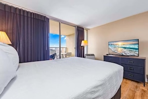 Hotelkamer met een bed, televisie, bureau met lades, stoel en uitzicht op de stad.