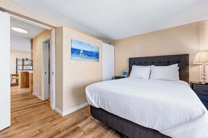 Une chambre d’hôtel avec un grand lit, une table de chevet, un tableau représentant un voilier et un plancher en bois.