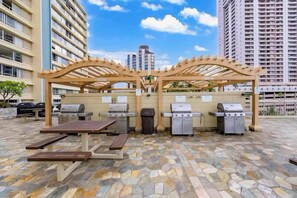Un espace extérieur aménagé avec une pergola, des barbecues et une table de pique-nique.