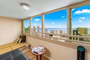 Un balcon avec vue sur la ville, une petite table avec une télécommande et un coin salon confortable avec des coussins.