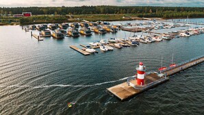 Ein Yachthafen mit mehreren angestaubten Booten, ein markanter roter und weißer Leuchtturm und eine Anlegestelle, die sich ins Wasser erstreckt.