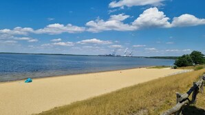 Ein Strand mit einer Holzlattenveranda, sandigem Ufer und blauem Himmel mit Wolken.