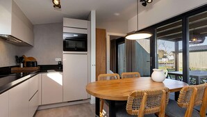 A modern kitchen with white cabinets, a black countertop, and a round wooden dining table with wicker chairs. - Waterfront Retreat, Friesland (Delfstrahuizen)