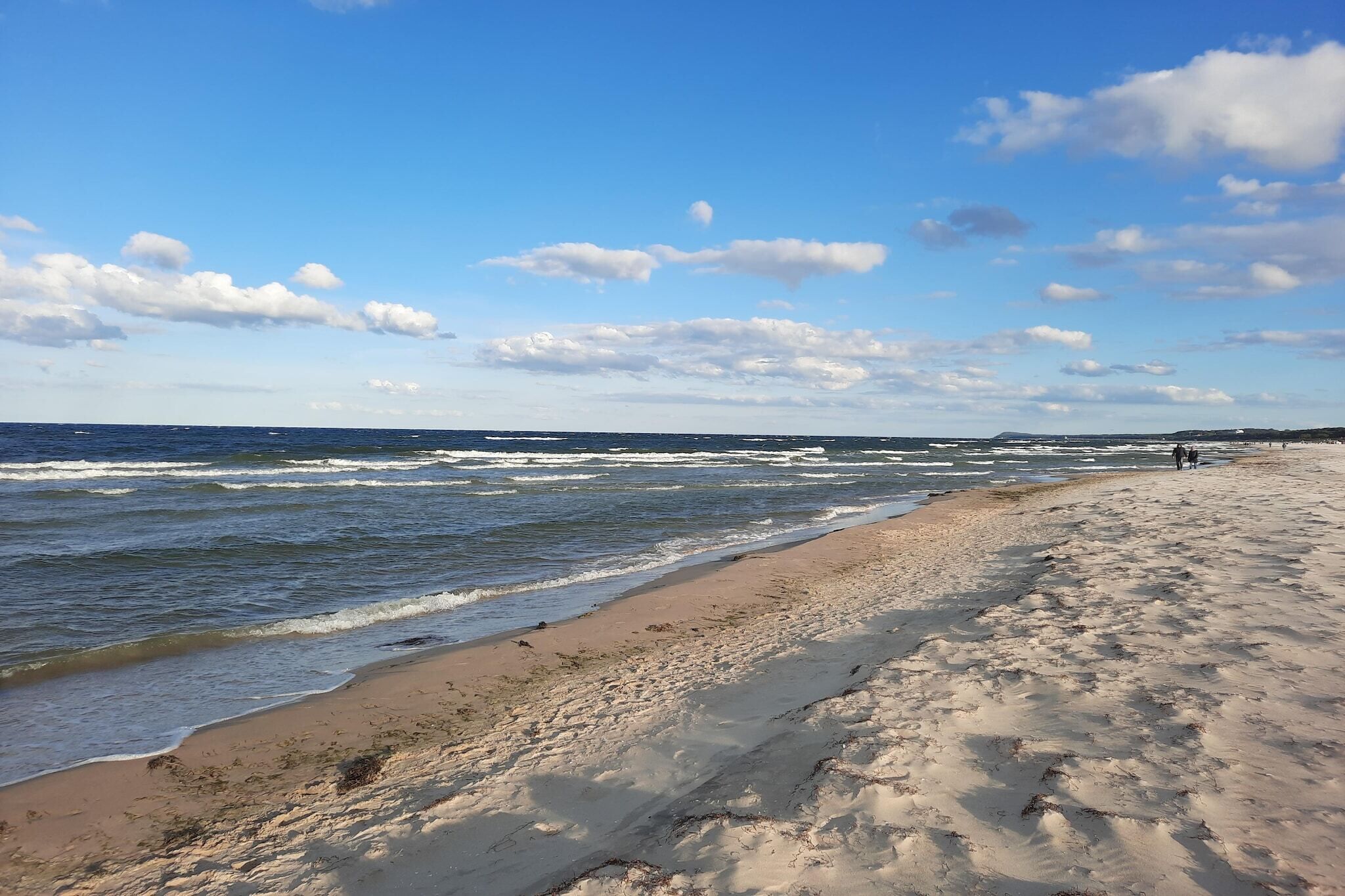Ein Strand mit Wellen, blauem Himmel und einer fernen Küste.