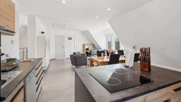 Eine moderne Küche mit einer zentralen Kochinsel, einem Essbereich mit Tisch und Stühlen sowie einer Treppe zu einer oberen Ebene.