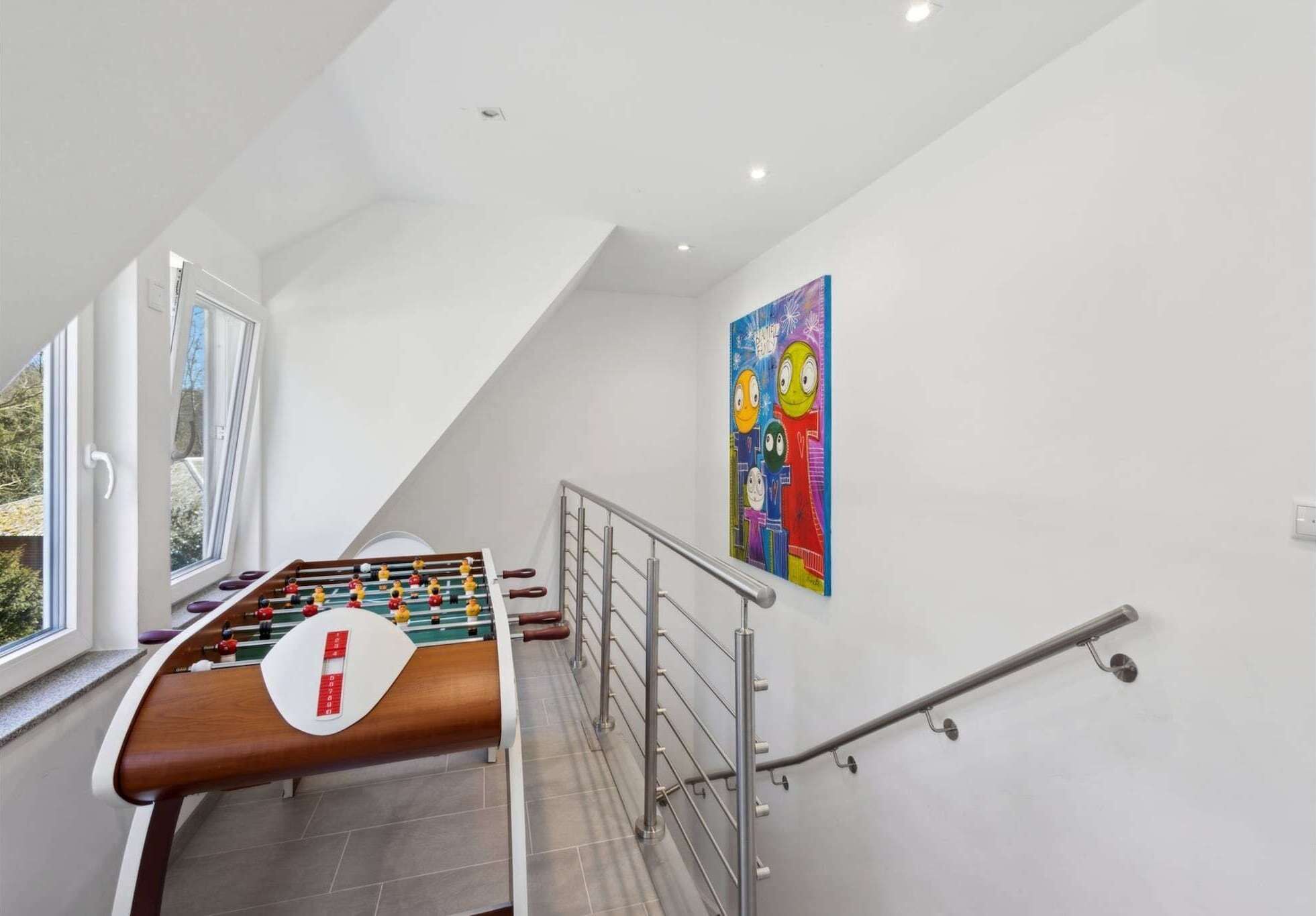A foosball table in a room with a sloped ceiling, a window, and a colorful painting on the wall.