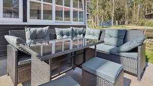 Un patio con mobili in vimini, un tavolo con piano in vetro e vista su una casa con ampie finestre.