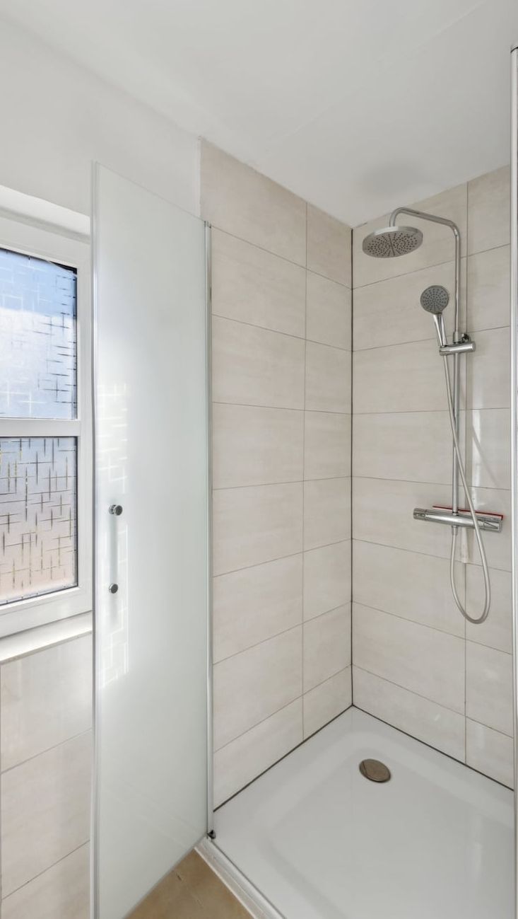 A modern shower with a glass door, a showerhead, and a drain.