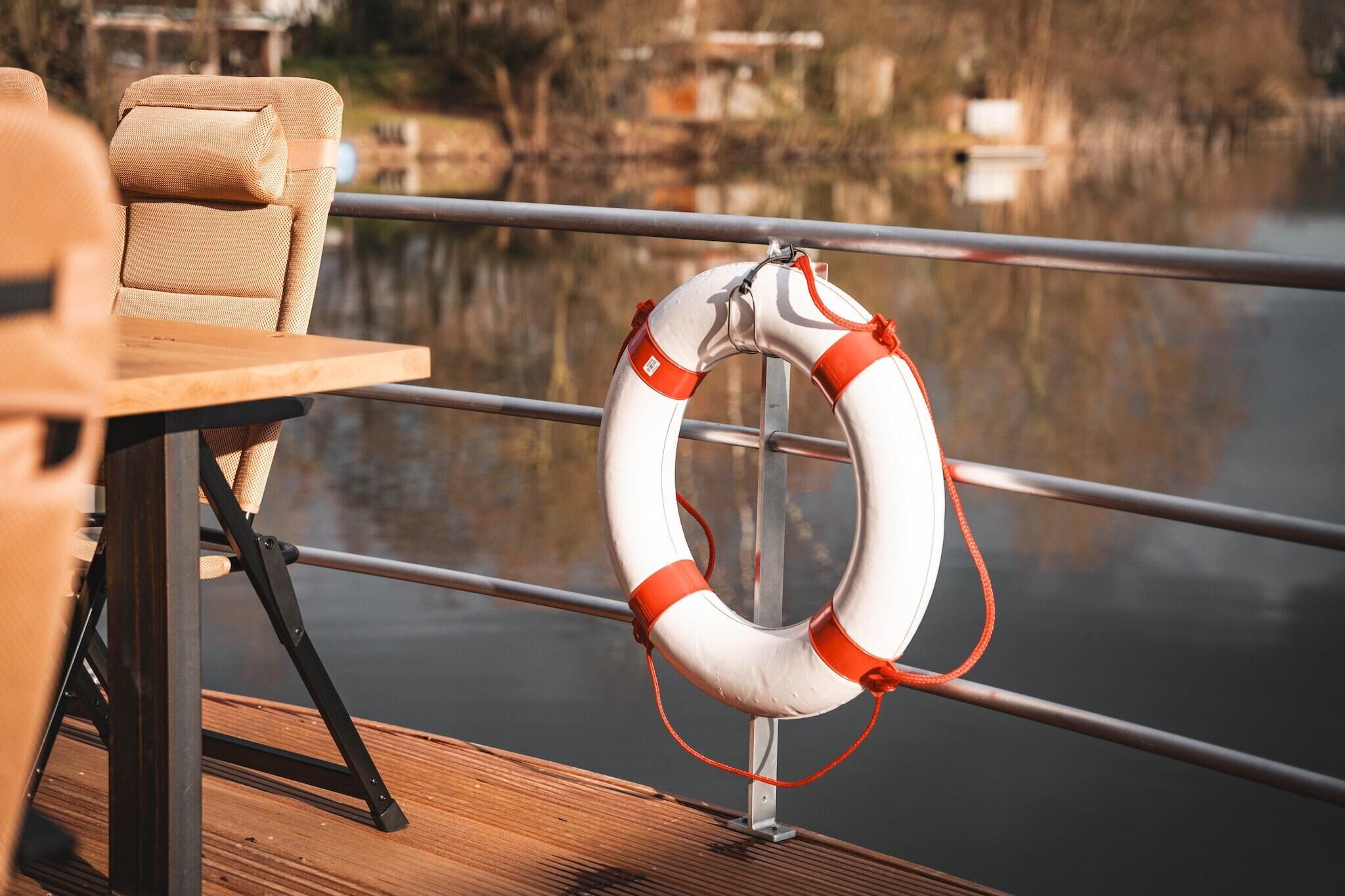 A lifebuoy attached to a metal railing on a wooden deck overlooking a body of water.
