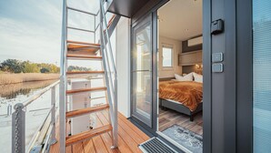 A modern bedroom with a large bed, a wooden deck, and a glass door leading to a balcony.