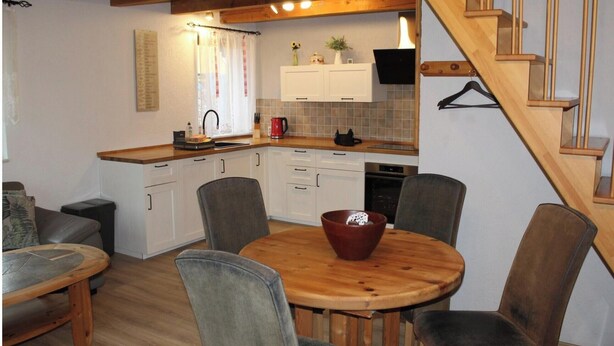 A compact kitchen with white cabinets, a wooden dining table, and a staircase. - Ferienhaus in Rethwisch (Rethwisch)