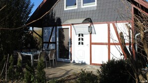 A two-story house with a grey roof, white trim, and a small front porch with a table and chairs. - Ferienhaus in Rethwisch (Rethwisch)