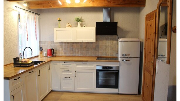 Een keuken met witte kastjes, een houten aanrechtblad, een inbouwoven en een koelkast.