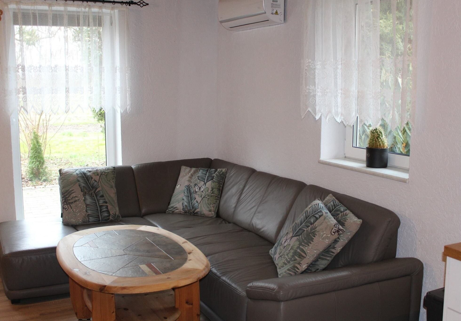 A modern living room with a curved grey sofa, patterned cushions, a round wooden coffee table, and a window with a potted plant.