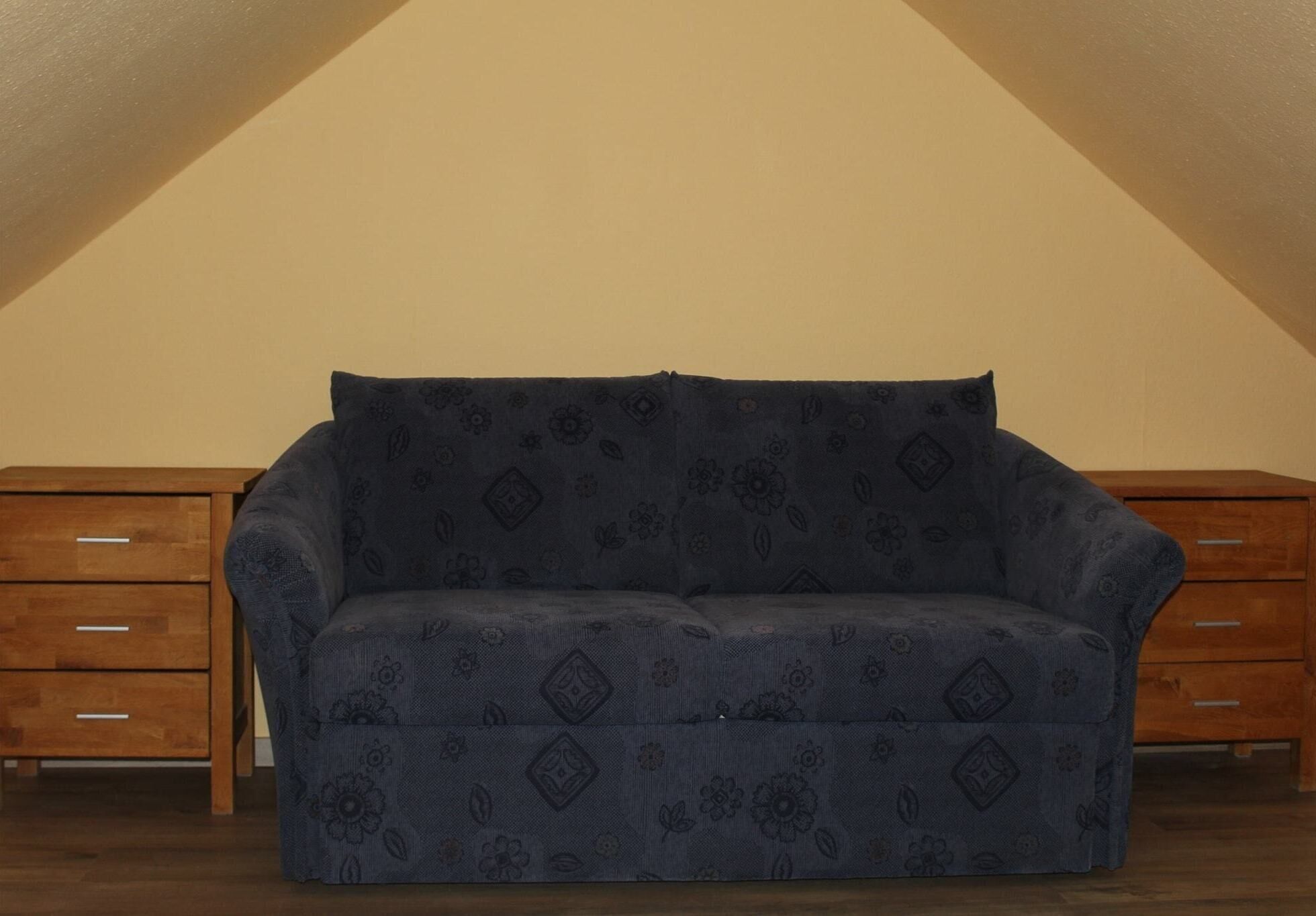 Un sofá azul con estampado floral en una habitación con muebles de madera y techo inclinado.