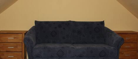Un sofá azul con estampado floral en una habitación con muebles de madera y techo inclinado.
