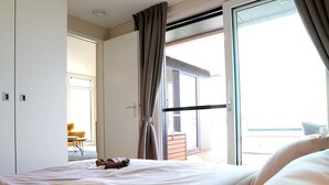 A hotel room with a bed, a sliding glass door to a balcony, and a small table with a chair.