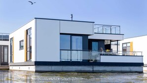 A modern floating house with a balcony, large windows, and a clear sky.