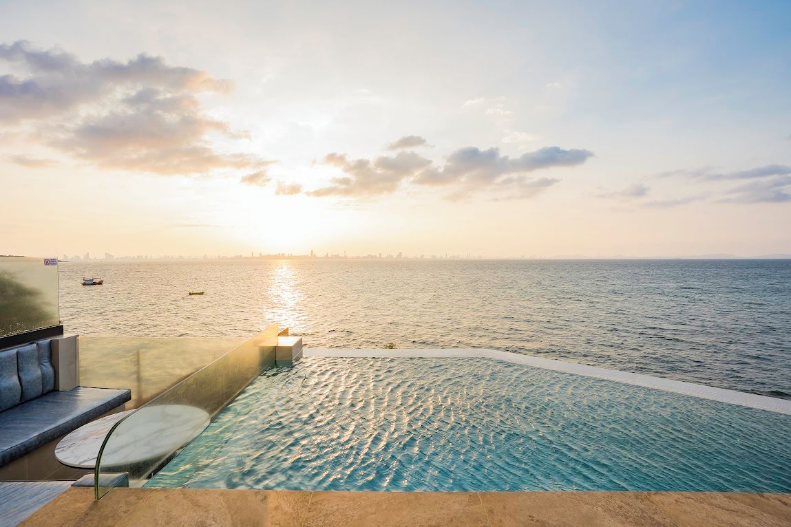 A infinity pool with a view of the ocean and a city skyline at sunset.