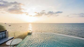 A infinity pool with a view of the ocean and a city skyline at sunset.