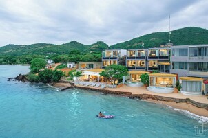 Una propiedad costera con piscina, un kayakista y varios edificios modernos con zonas de estar al aire libre.