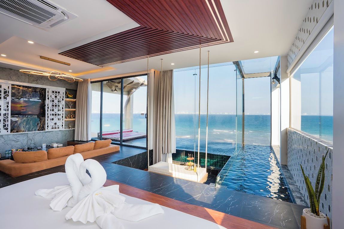A modern hotel room with a large window overlooking the ocean, a private infinity pool, and a seating area with a sofa.