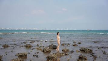 Una persona de pie en una playa rocosa, con un horizonte urbano al fondo.