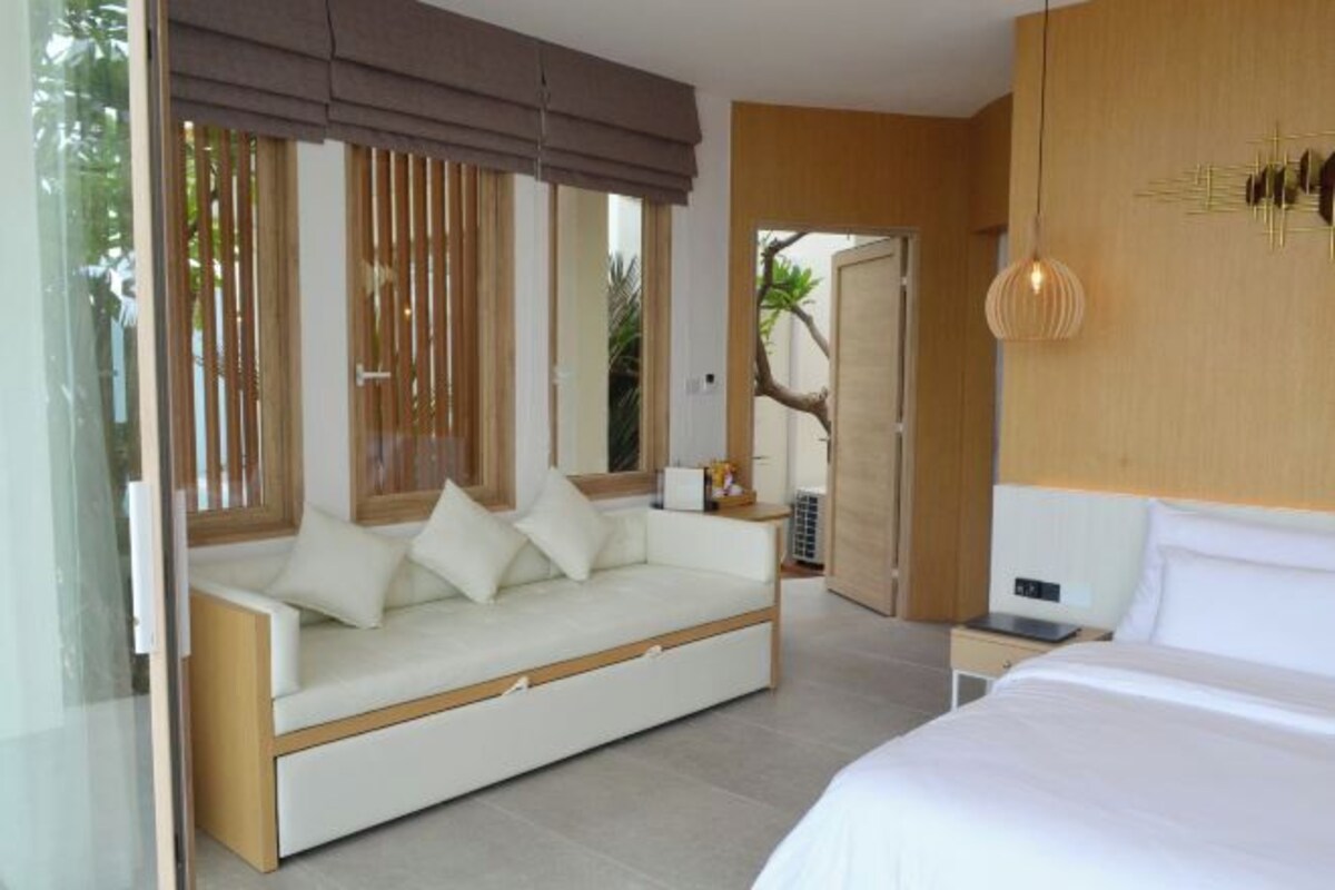 A modern hotel room with a sofa bed, a separate bed, a bedside table, and a large window with blinds.