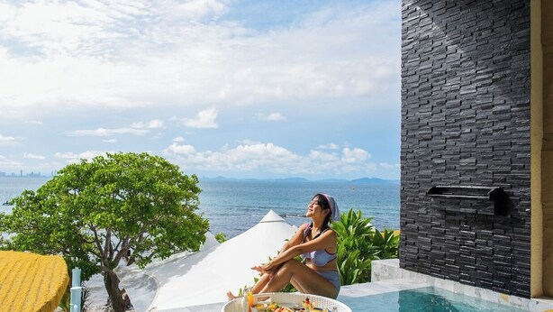 Une piscine avec une personne assise sur une plateforme flottante, un ventilateur de plafond et une vue sur la mer.