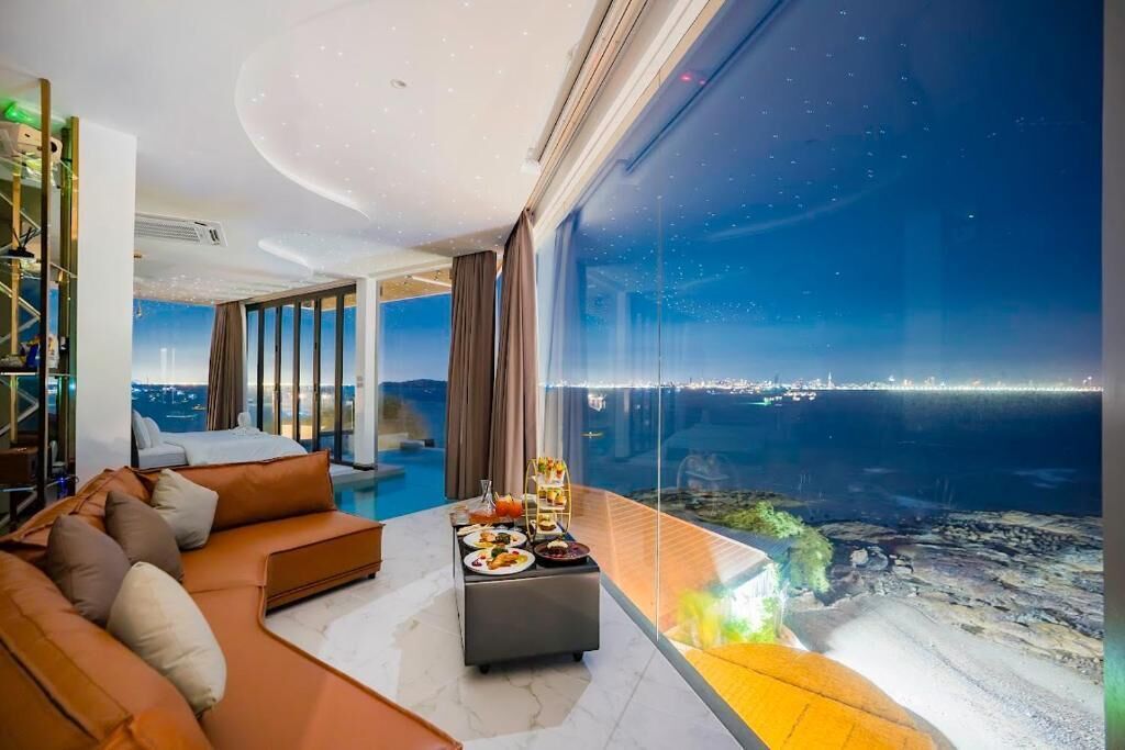 Una sala moderna con un ventanal que ofrece vistas a la costa, un sofá y un comedor con una mesa dispuesta para una comida.