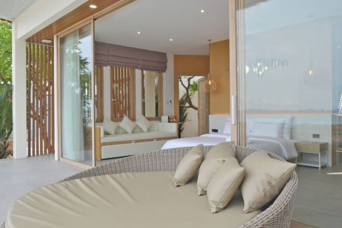 A modern bedroom with a large bed, a sofa, and a wicker chair.