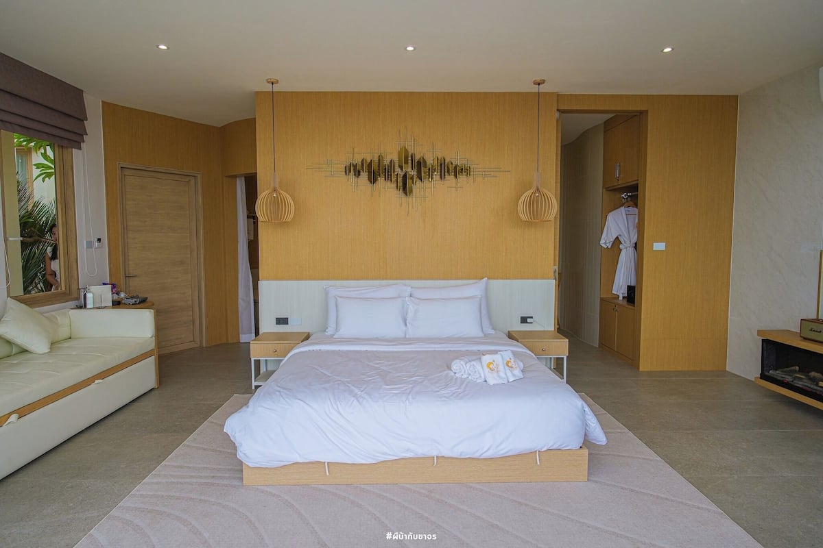 Une chambre moderne avec un grand lit, une table de chevet, une commode, une armoire en bois et une salle de bain visible à travers une porte ouverte.
