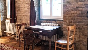 A room with a brick wall, a wooden table, two wooden chairs, a radiator, and a window with curtains. - Poetic Studio with Garden (Berlin)