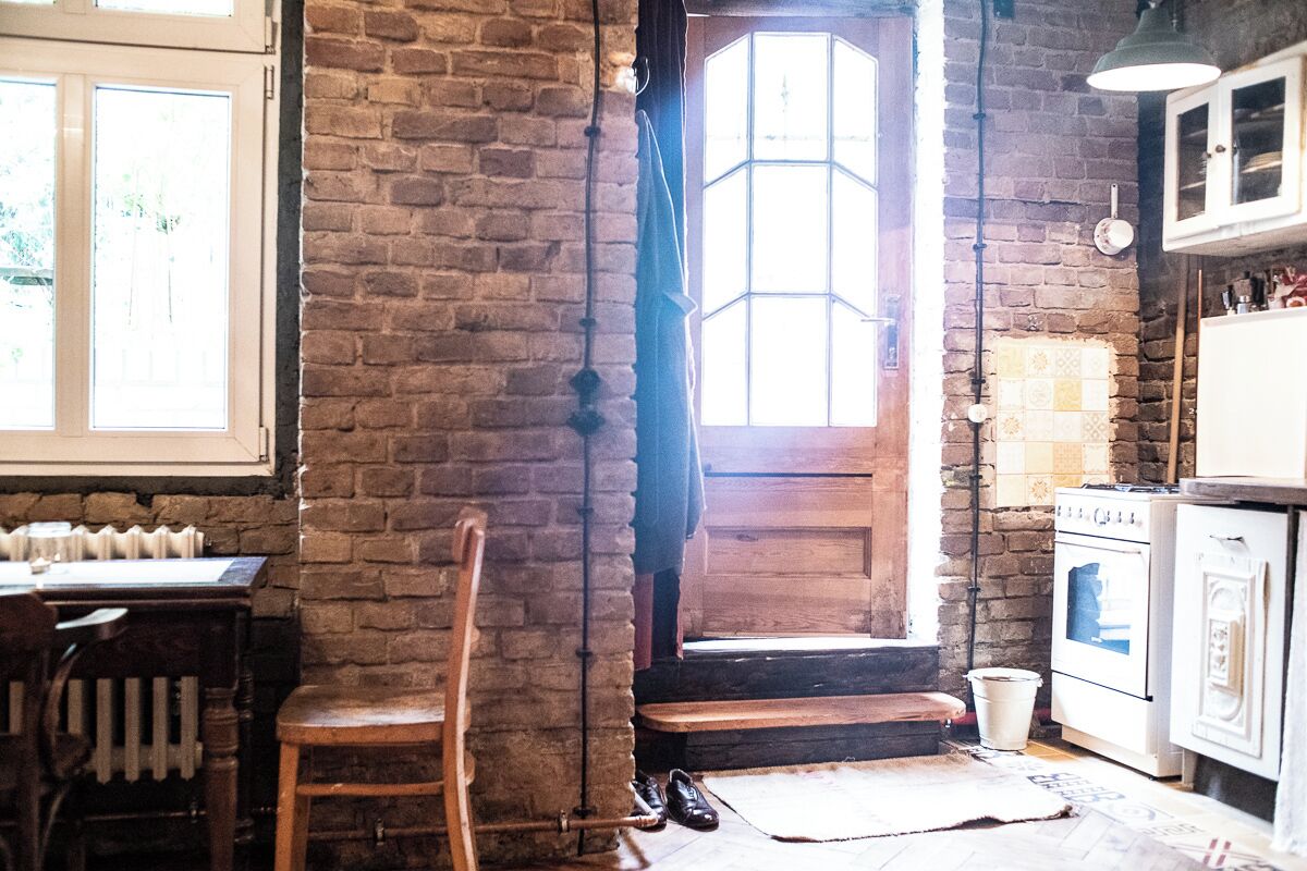 A rustic kitchen with a brick wall, wooden door, and white cabinets.