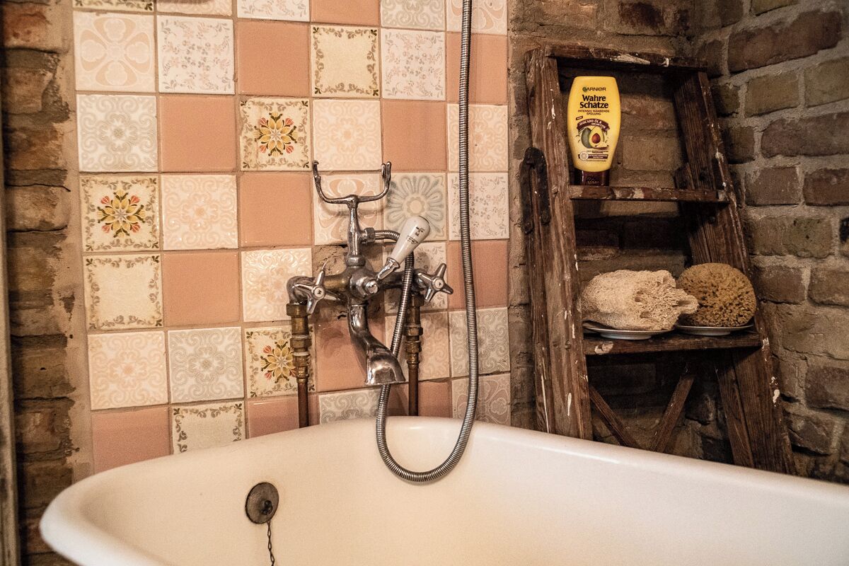 Une salle de bain avec une baignoire, une douche et une étagère où est posé du pain.