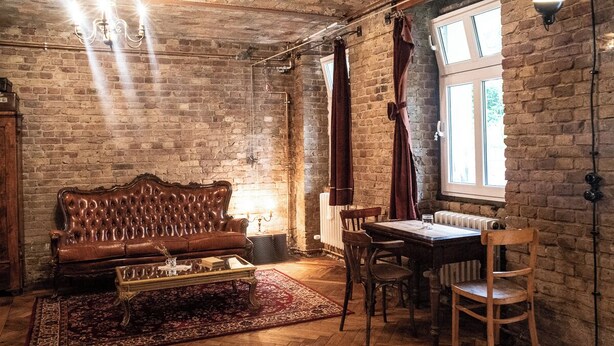 A cozy living room with a brown leather sofa, a wooden coffee table, and a dining table with chairs. The room has exposed brick walls and a large window with curtains. - Poetic Studio with Garden (Berlin)