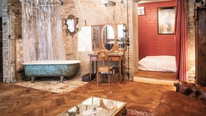 A room with a vintage bathtub, a wooden desk, a leather sofa, and a bed with a red wall. - Poetic Studio with Garden (Berlin)