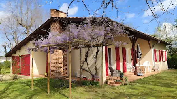 Ein Haus mit Ziegelkamin, roten Fensterläden und einer Laube mit Gartenmöbeln.