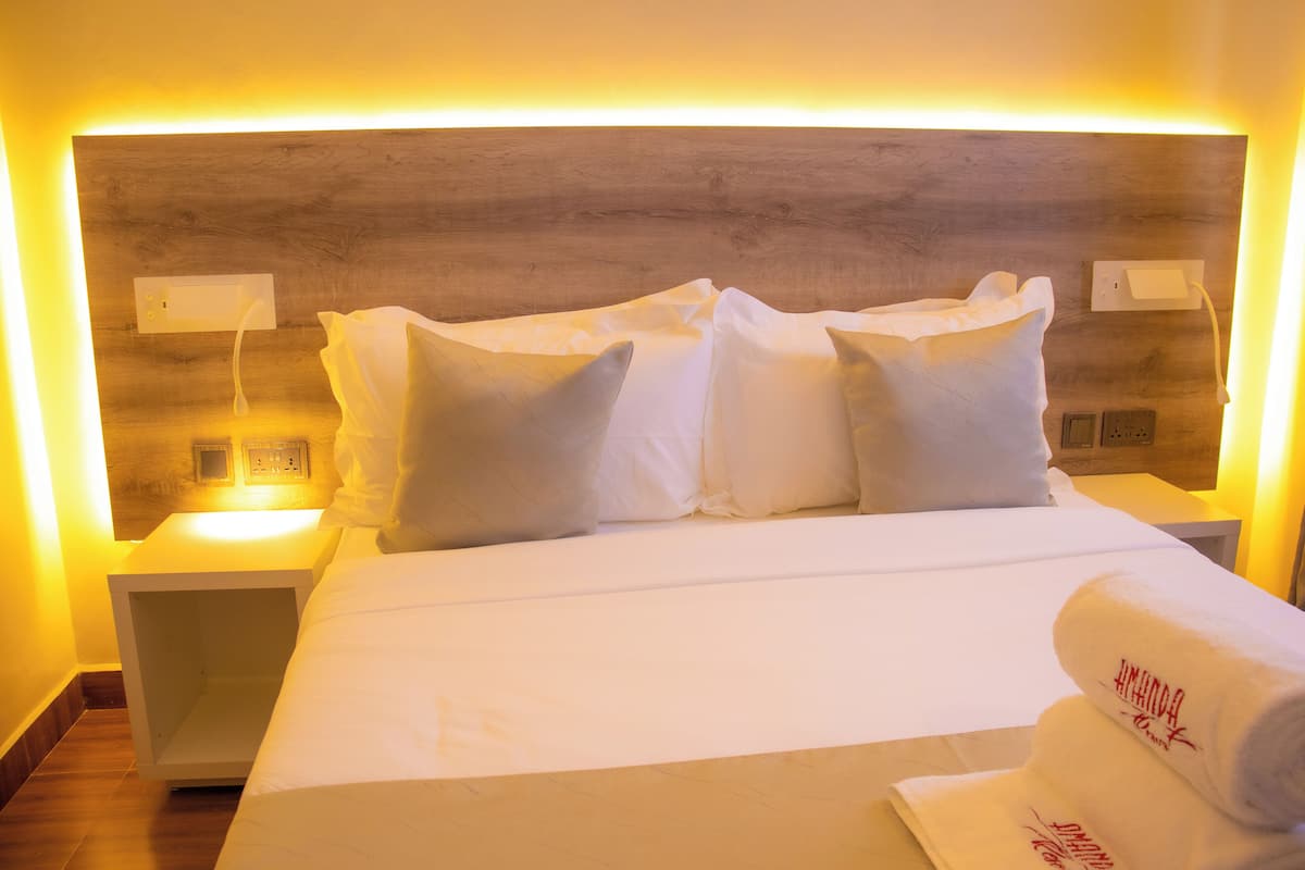 A neatly made bed with white linens and pillows, a wooden headboard, and bedside lamps.