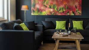A modern living room with a dark sofa set, a wooden coffee table with glasses and food, and a floor lamp. - Gîte chez Alice et Marcel: sauna, cabin, chicken coop, bicycles & garden. (Saulxures-sur-Moselotte)