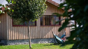A wooden house with a stone foundation, a large window, and a hammock in the yard. - Gîte chez Alice et Marcel: sauna, cabin, chicken coop, bicycles & garden. (Saulxures-sur-Moselotte)