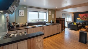 A modern kitchen with wooden cabinets, a gas stove, and a large window. - Gîte chez Alice et Marcel: sauna, cabin, chicken coop, bicycles & garden. (Saulxures-sur-Moselotte)