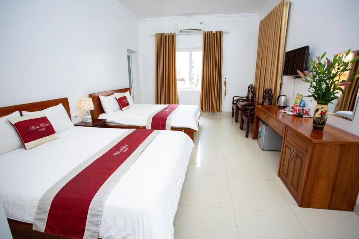 A hotel room with two beds, a wooden desk, a television, and a window with curtains.
