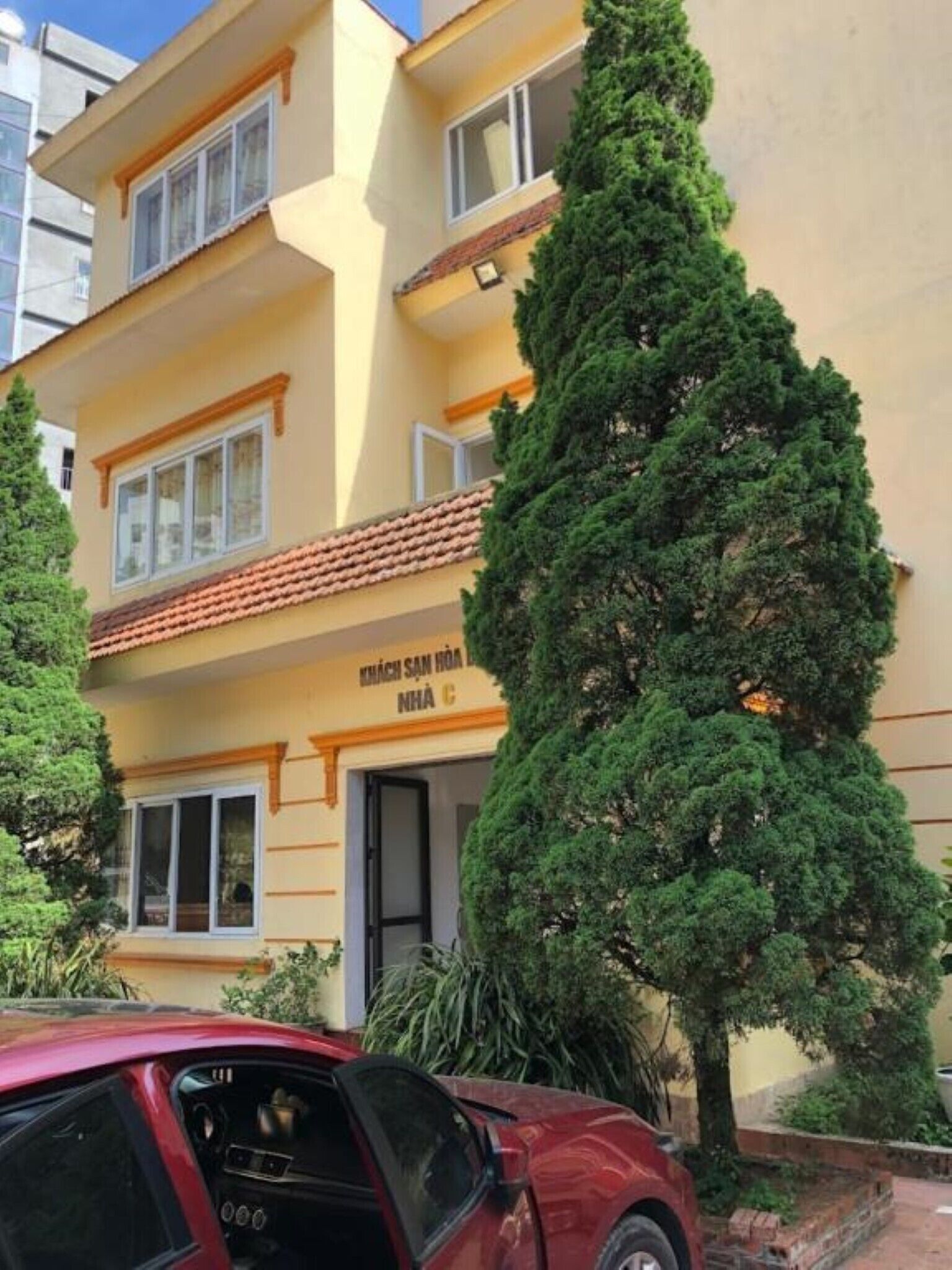A multi-story building with a yellow facade, a visible entrance, and a red car parked in front.