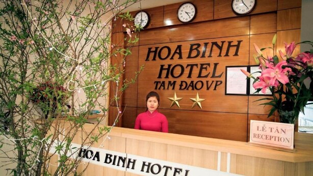Mostrador de recepción del Hotel Hoa Binh con relojes, un letrero para la recepción y una planta decorativa.