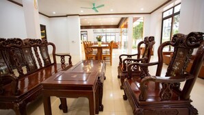 Un comedor con muebles de madera ornamentados, un ventilador de techo y ventanas amplias.
